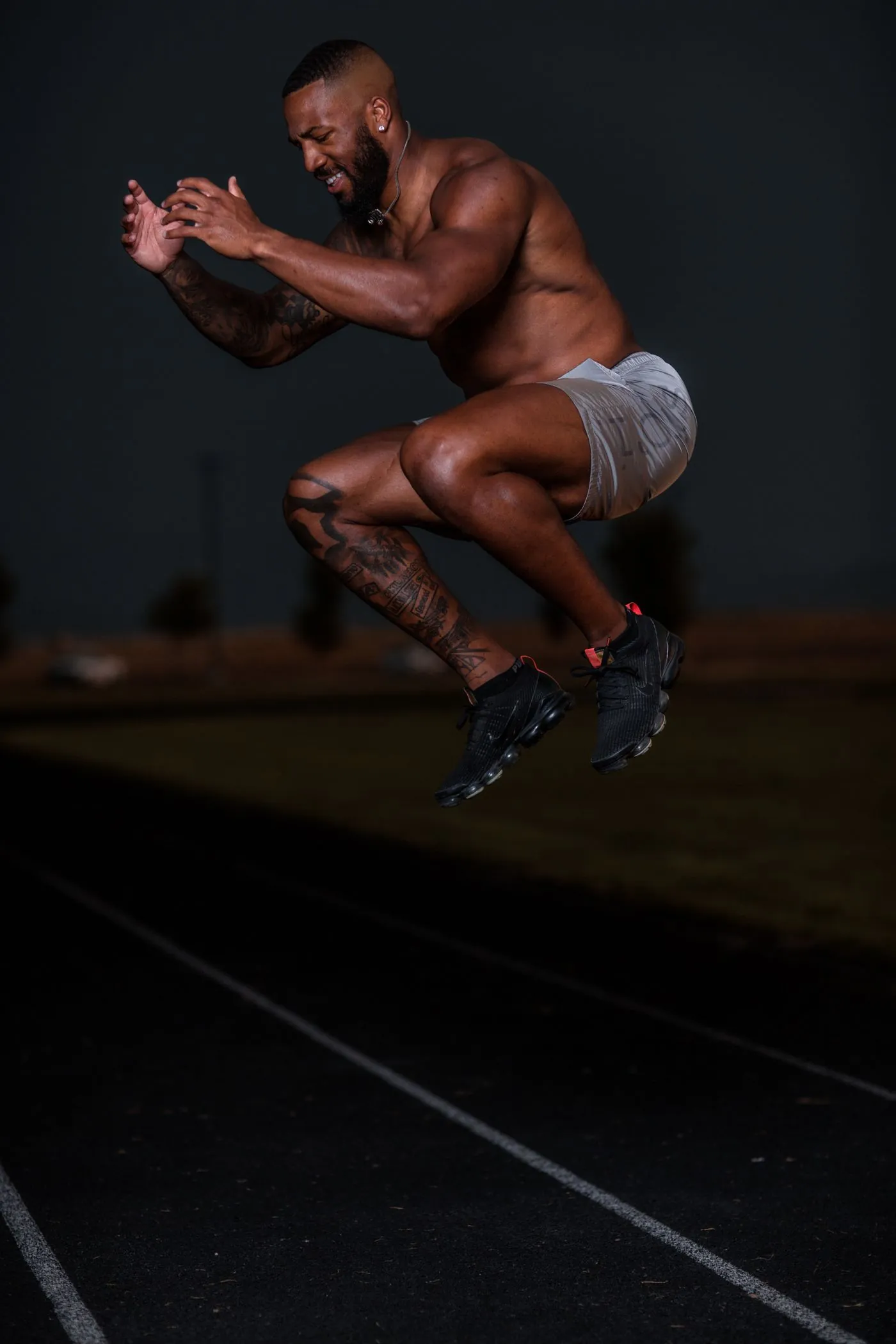 An athlete mid-air in an explosive tuck jump on an outdoor running track