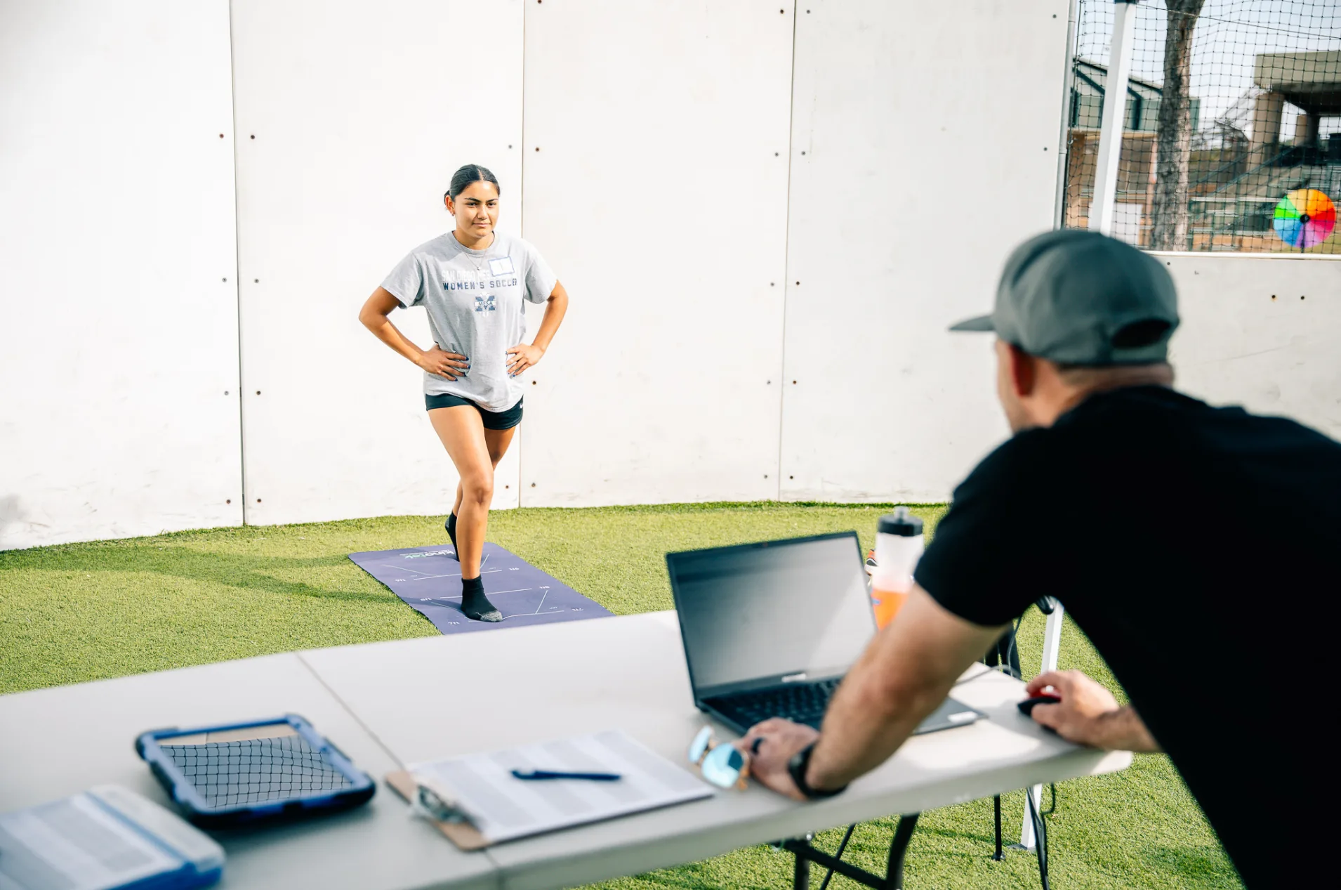 An athlete holds a single-leg movement screen while an IMTI coach reads her results on a laptop